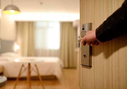 Man's hand holding a door handle opening the door to reveal inside a modern hotel room